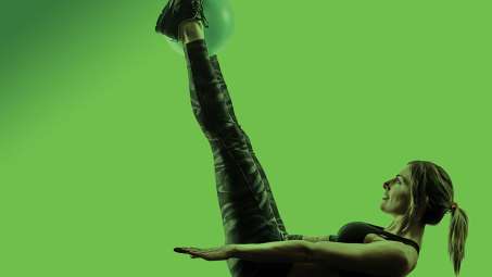 presenting as woman in workout tights laying on back doing high leg lift all with green background and green filter