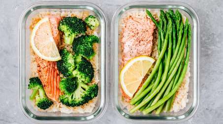 two glass containers filled with food. one with chicken and broccoli the other with salmon and asparagus. 