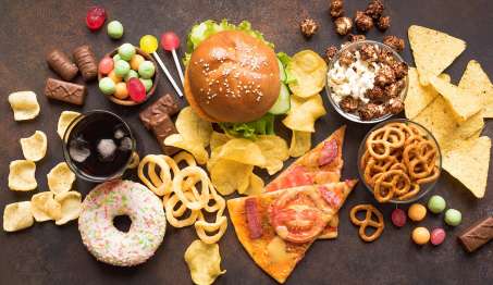 counter filled with many versions of junk food including pizza, doughnuts, potato chips, burger, candy, etc...