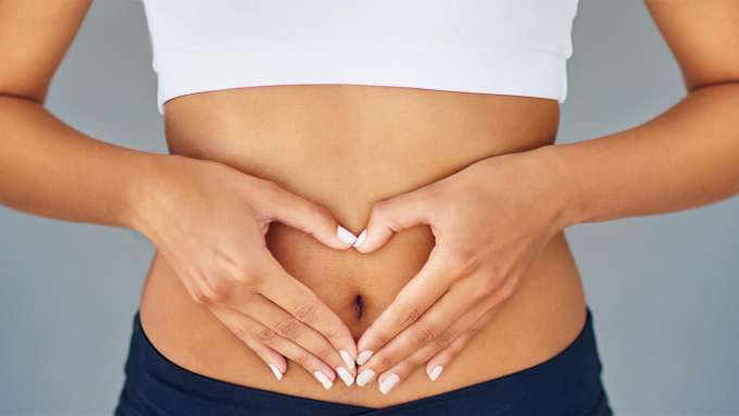 close up of a person with a bare midriff and hands shaped like a heart around navel