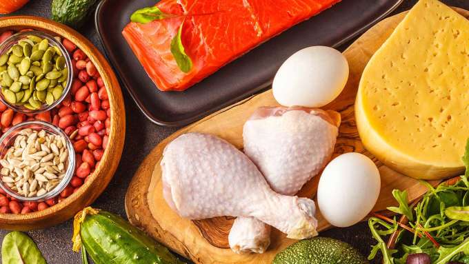 food spread out on a table including a wooden bowl full of grain/beans, two raw chicken legs, two eggs, and a piece of raw fish