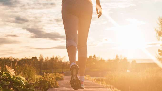 lower half of a person running into the sun on an outdoor path