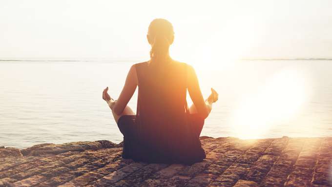 silhouette of presenting as woman from behind sitting on beach in a yoga position