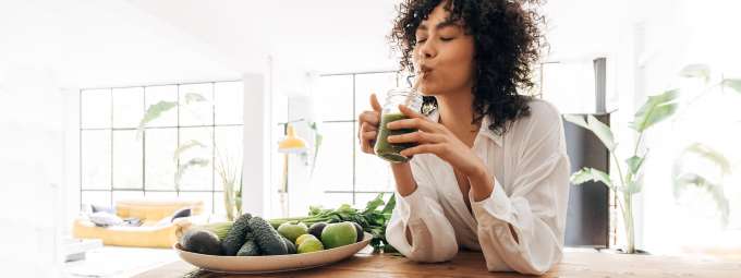 dark skinned female presenting person drinking a green smoothie