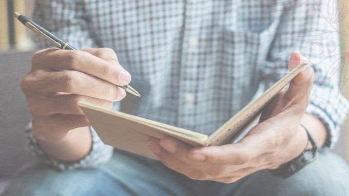 light skinned person writing in a journal 