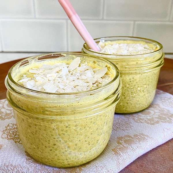 two servings of golden milk chia seed pudding shown in canning jars, one with a spoon in it sitting on a light placemat on a wood table