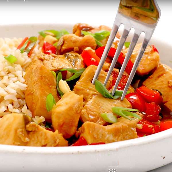 white bowl with kung pao chicken and rice with a fork ready to dig into dish