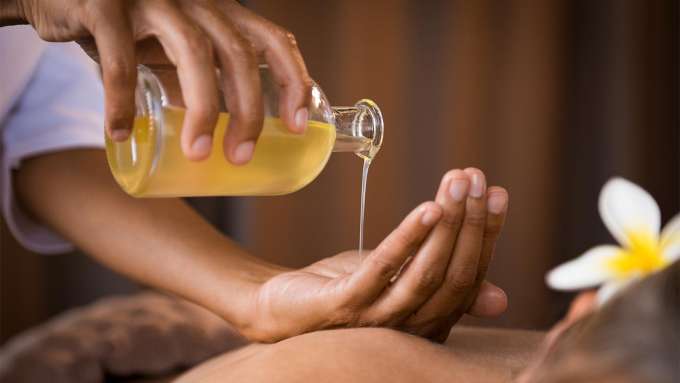 dark skinned person pouring massage oil into their hand from a glass bottle