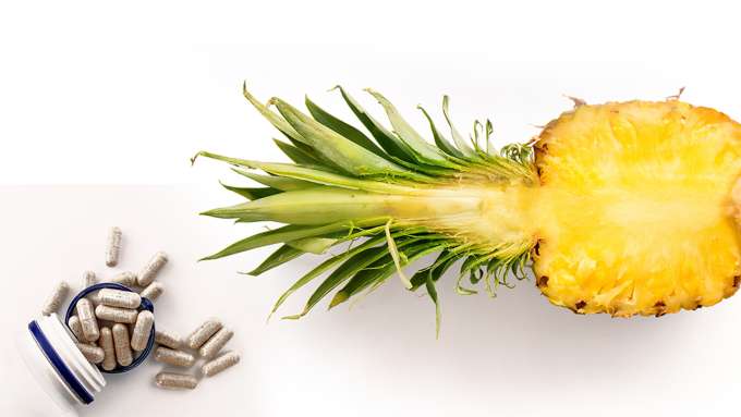 bottle of supplements spilled out next to a pineapple half section with top 