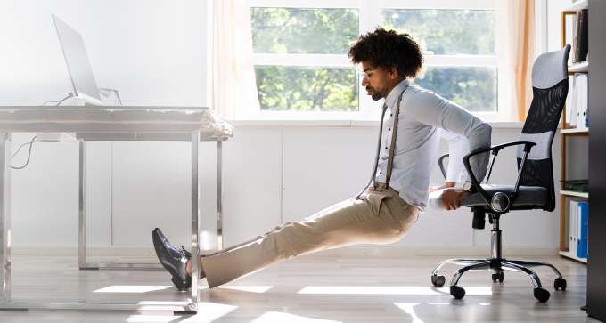 dark skinned male presenting person stretching using his desk chair  