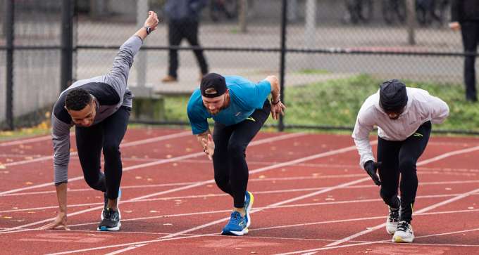 group of male presenting people lined up on a running track starting line