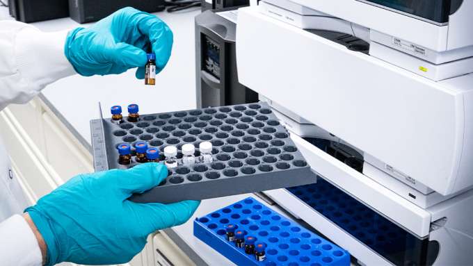 blue gloved hands holding small brown vitals to put into a machine to test