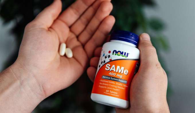 hands holding SAMe bottle and tablets