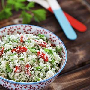 A white ceramic bowl with red and blue floral decorations is filled with Cauliflower Couscous
