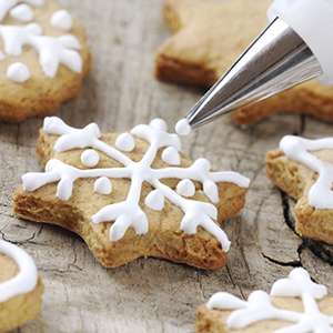 Several snowflake shaped gingerbread cookies on a wooden table being decorated with Flat Icing.