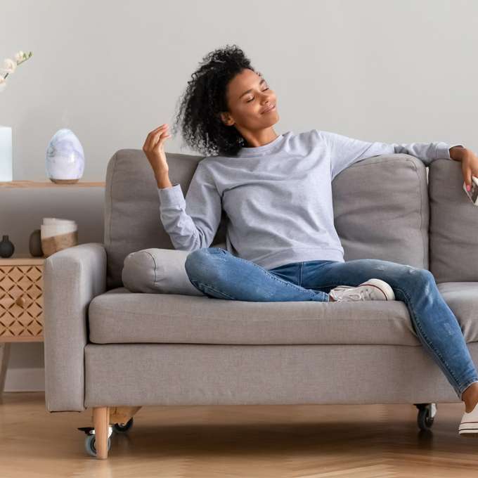 dark-skinned, female-presenting person on a couch, smelling the air