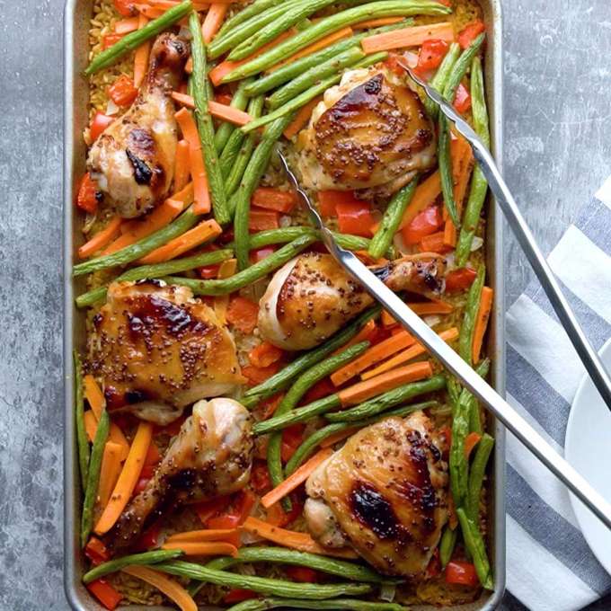 A sheet pan filled with chicken thighs, green beans, and carrots.