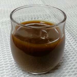 A closeup of a drinking glass filled with a serving of dark brown Spiced Pumpkin Syrup