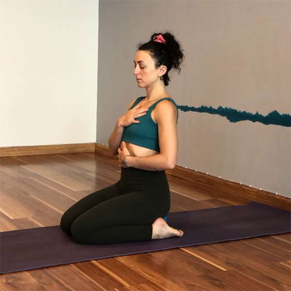 presenting as woman with black yoga pants and green sports top kneeling on a mat in a room with wood floors and white walls