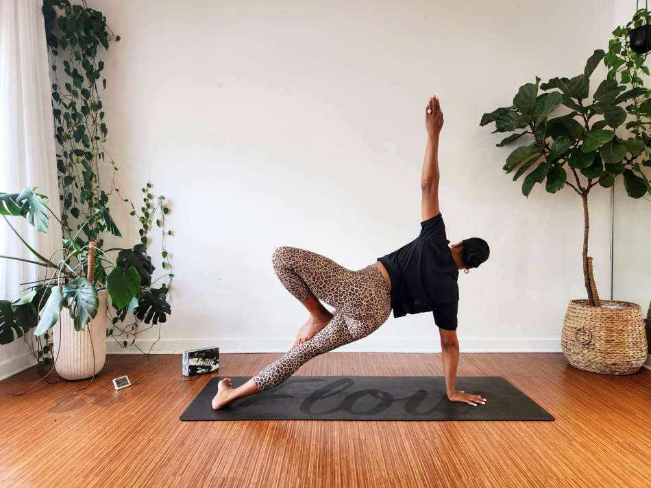 medium skin toned female presenting person doing a yoga pose on a black yoga mat 