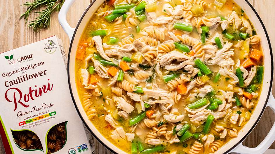 chicken vegetable noodle soup in a bowl next to a box of Living NOW Cauliflower Rotini