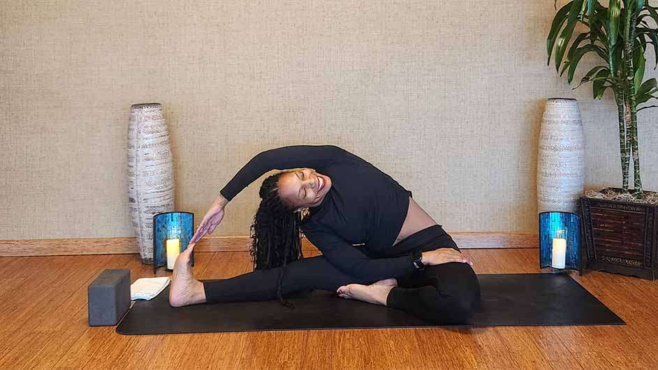 dark skin female presenting person stretching on a yoga mat in all black