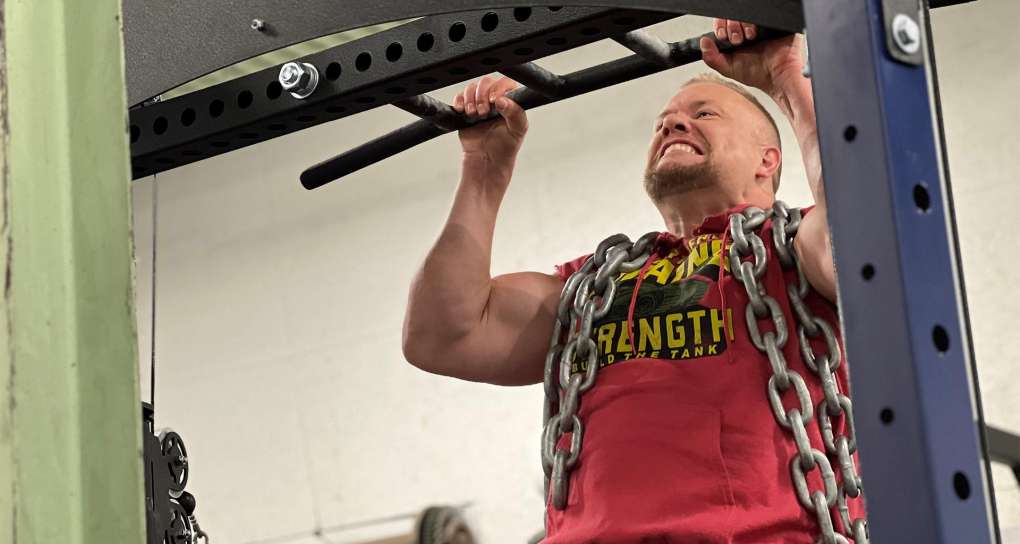 Matt Mulligan doing pull-ups with heavy chain draped over him. 